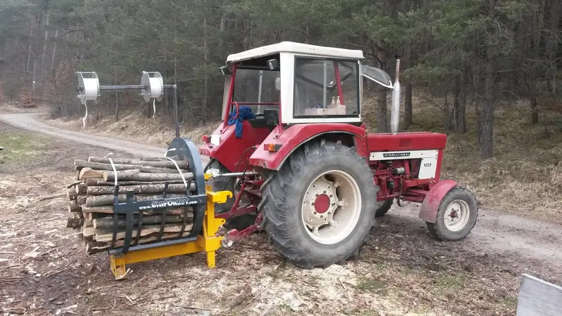Roter Traktor mit Bündelgerät und frisch gebündeltem Meterholz am Waldweg