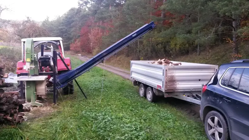 Säge mit Förderband füllt einen Anhänger hinter einem Auto