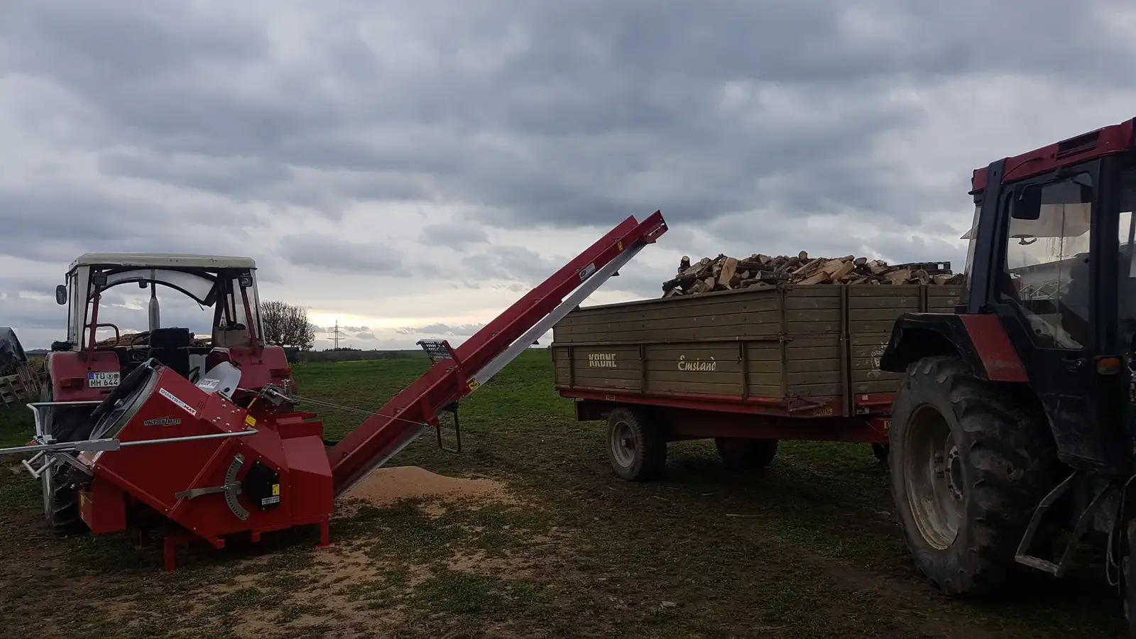 Traktor mit beladenem Holzanhänger und Säge auf dem Feld