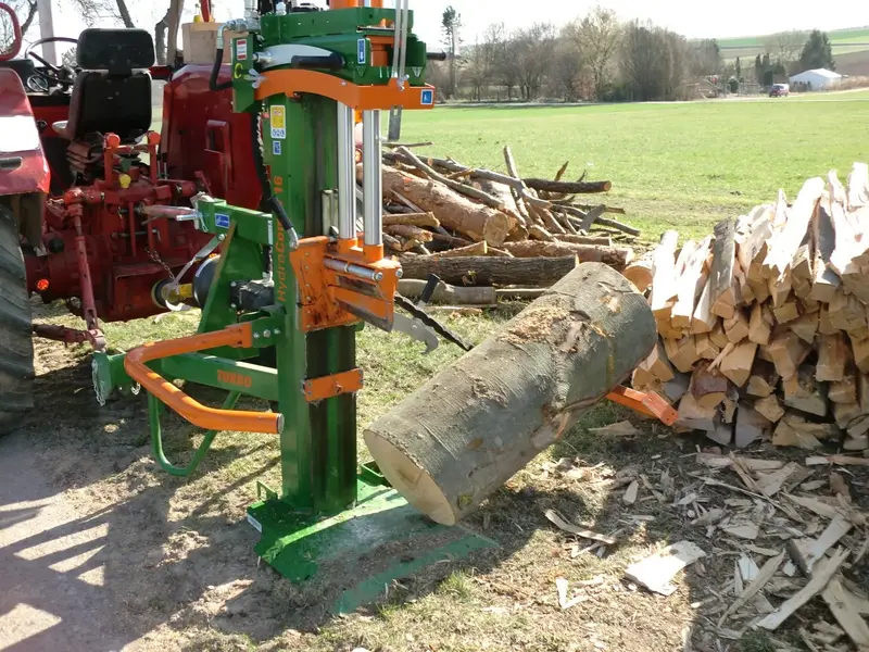 Grüner Holzspalter am Traktor mit einem dicken Stammstück